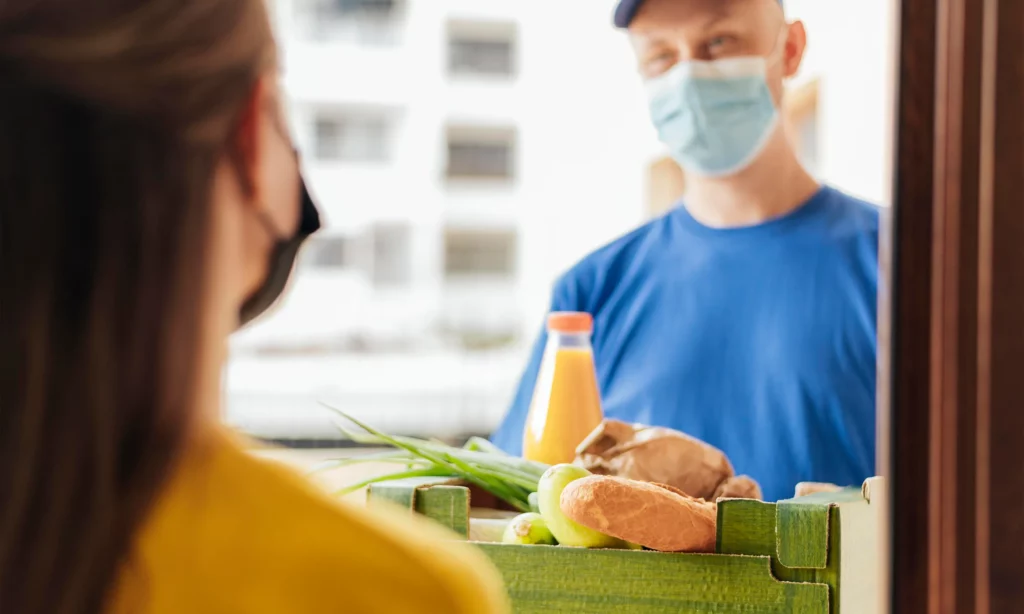 how to survive beyond COVID-19 a deliveryman handing over a box filled with bread, vegetables, and juice